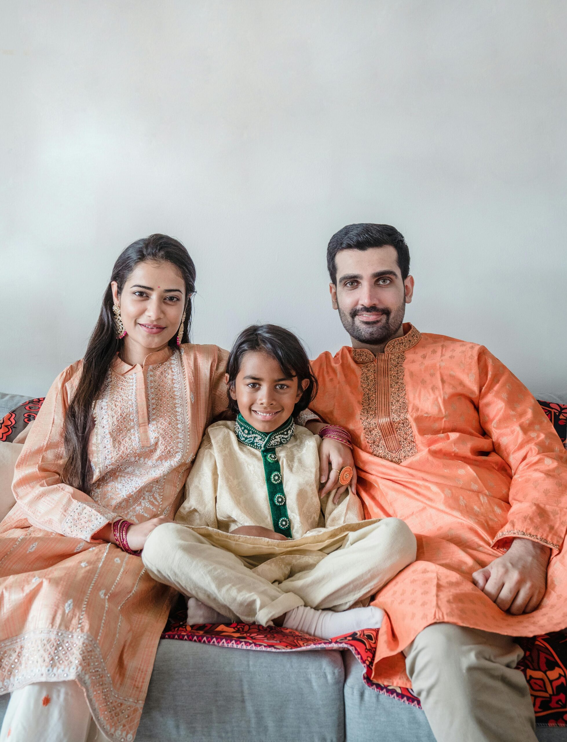 A joyful Indian family seated on a sofa in traditional attire, expressing happiness.